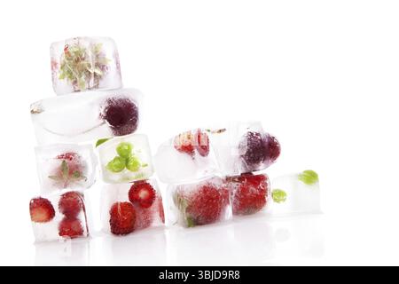 Himbeeren, Erdbeeren, Kirschen und grüne Erbsen gefroren in Eiswürfeln isoliert auf weißem Hintergrund. Frisches Sommerobst. Gesunde Ernährung Stockfoto