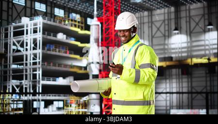 Afroamerikaner In Hardhat Hält Blueprints Auf Der Baustelle. Stockfoto