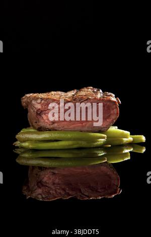 Mittelgroßes, seltenes Rindersteak mit Bohnen auf schwarzem Hintergrund Stockfoto