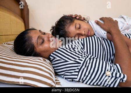 Eine Mutter und ihre Tochter verbringen einen zärtlichen Moment, während sie auf einem gemütlichen Bett in einer ruhigen Umgebung schlafen. Stockfoto