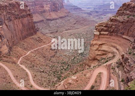 Eine gewundene Feldstraße schlängelt sich durch die riesigen, zerklüfteten Canyons, umgeben von hohen Felsformationen und trockenem Gelände. Das Sonnenlicht hebt die Natu hervor Stockfoto