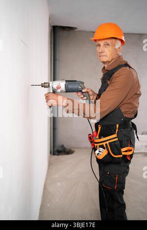 Builder verwendet Bohrer, um ein Loch in der Wand zu machen. Konzept für Bau-, Reparatur- und professionelle Renovierungsarbeiten Stockfoto