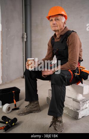 Kaffee in den Händen eines Bauarbeiters, der auf der Baustelle eine Pause hat. Alter Bauarbeiter oder Bauarbeiter in neuem Haus Stockfoto
