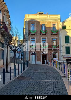 Sesimbra, Portugal. 20. Dezember 2024 Ein dreistöckiges Gebäude mit klassischen Azulejo-Keramikfliesen, Balkonen mit grünen Girlanden, neben narro Stockfoto