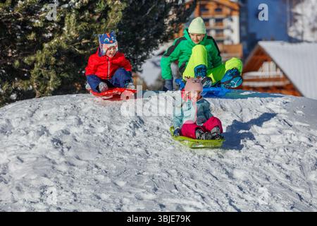 Kinder lachen, während sie eine schneebedeckte Piste hinunterfahren, Winterspaß Stockfoto