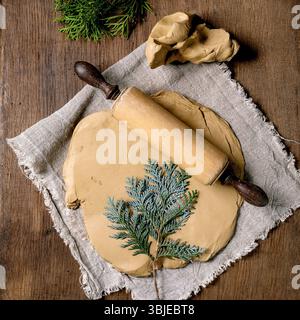 Dekorkeramik. Eine gerollte Platte aus roher gelbem Ton mit Prägung von Thuja-Zweigen liegt auf grobem Stoff auf Holztisch. Öko-Einrichtung. Spannstift, Werkzeug Stockfoto