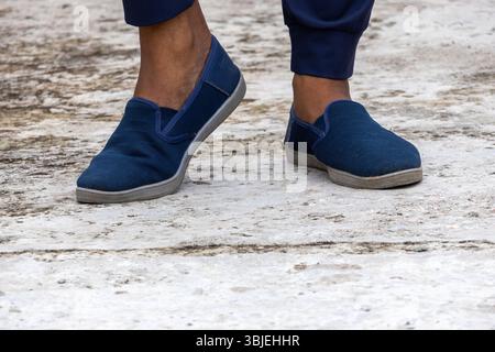 Nahaufnahme des Fußes des Mannes mit marineblauen Turnschuhen auf Beton. Bequeme, stylische, sportliche Schuhe. Stockfoto