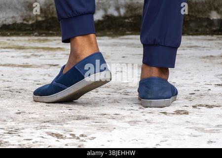 Männlicher Fuß mit marineblauen Sneakers auf Beton. Stylische, modische, bequeme Herrenschuhe, Nahansicht hinten. Stockfoto