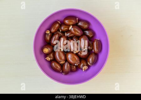 Blick von oben auf Lychee (Litchi chinensis) Obstsamen in einer Plastikschale auf Holz. Stockfoto