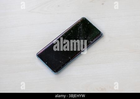 Smartphone mit gerissenem Bildschirm auf hölzernem Hintergrund. Handy beschädigt, Display kaputt. Stockfoto