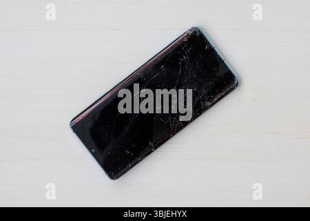 Smartphone mit gerissenem Bildschirm auf hölzernem Hintergrund. Draufsicht des beschädigten Mobiltelefondisplays. Kaputtes Handy muss repariert werden. Stockfoto