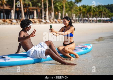 Vielfältige Paare verbunden, mit Technologie und sozialen Medien, während Sie Momente am Strand genießen Stockfoto