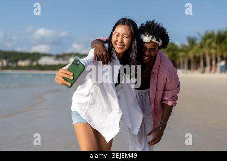 Vielfältige Paare verbunden, mit Technologie und sozialen Medien, während Sie Momente am Strand genießen Stockfoto