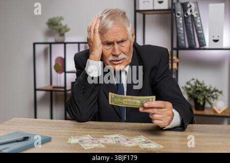 Kaukasischer Senior-Geschäftsmann Freelancer zählt Bargeld zu wenig Geld. Finanzkrise. Konkurs. Armut und Elend. Großvater im Anzug sitzt am Tisch im Büro. Stockfoto