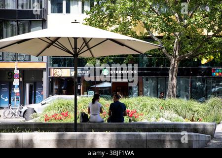 15. Juni 2025, Berlin, Berlin, Deutschland: Am Sonntag, 15. Juni 2025 sitzt ein Paar unter einem Sonnenschirm auf dem Bürgersteig gegenüber einem Starbucks in der Tauentzienstraße in Berlin. Das Paar blickt auf den â Eingang des cafÃ, während Touristen und Käufer durch den geschäftigen Einkaufskorridor in der Nähe der Kaiser-Wilhelm-Gedächtniskirche fahren. Die Tauentzienstraße ist nach wie vor eine der am stärksten befahrenen Geschäftsstraßen BerlinÂ. (Kreditbild: © Michael Kuenne/PRESSCOV via ZUMA Press Wire) NUR REDAKTIONELLE VERWENDUNG! Nicht für kommerzielle ZWECKE! Stockfoto