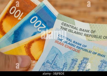 Geld von Israel und Iran. Geschäfts- und Finanzkonzept. Israelische Schekel und iranische Rials in der Hand. Gegenseitige Beziehungen und ihre Auswirkungen auf die Währung o Stockfoto