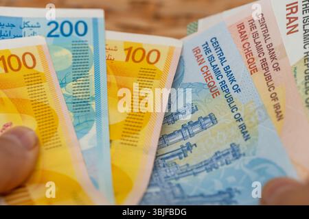 Geld von Israel und Iran. Geschäfts- und Finanzkonzept. Israelische Schekel und iranische Rials in der Hand. Gegenseitige Beziehungen und ihre Auswirkungen auf die Währung o Stockfoto