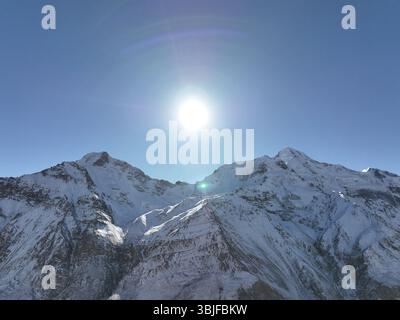 Die Sonne scheint hell über majestätischen, schneebedeckten Berggipfeln und schafft eine atemberaubende und ruhige Naturszene Stockfoto
