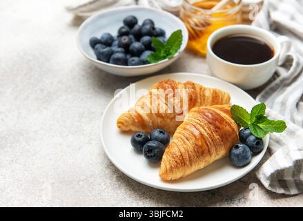 Frisch gebackene Croissants, serviert mit Heidelbeeren, Honig und Kaffee, die ein leckeres Frühstück bilden Stockfoto