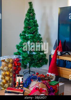 Grüner künstlicher Weihnachtsbaum im Wohnzimmer mit Kästen und Weihnachtsschmuck, bevor die festliche Dekoration beginnt Stockfoto