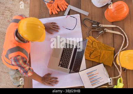 Blick von oben auf einen Bauarbeiter, der an einem Tisch steht und seinen Laptop in Thailand betrachtet Stockfoto