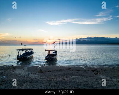 Zwei traditionelle Holzboote ankern bei Sonnenuntergang an einem tropischen Strand, Gili Air, Lombok, Indonesien Stockfoto