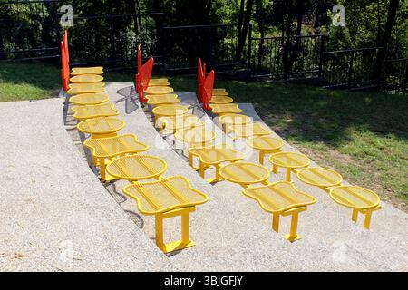 Reihen von hellgelben Metallsitzen mit abgerundeten Rücken und Netzflächen sind in einem geschwungenen Amphitheater im Freien angeordnet, das durch rote Geländer getrennt ist Stockfoto