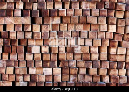 Ein großer Stapel von quadratisch geschnittenen Holzbalken ist mit der Querstruktur nach außen angeordnet und zeigt natürliche Holzmuster, Risse und warme Brauntöne Stockfoto