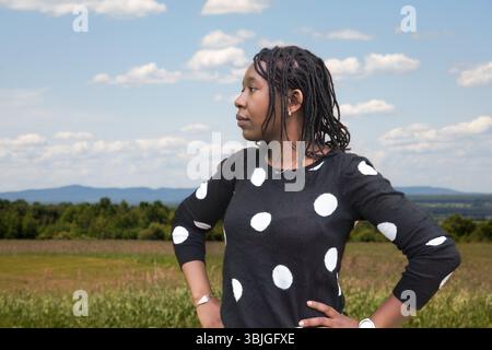 Porträt einer Frau mit natürlichen Dreadlocks im trendigen gepunkteten Topf, malerische Landschaft im Hintergrund Stockfoto