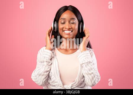 Porträt von lächelnden zurück Frau hört ihre Lieblingsmusik mit geschlossenen Augen, rosa Studio-Hintergrund Stockfoto