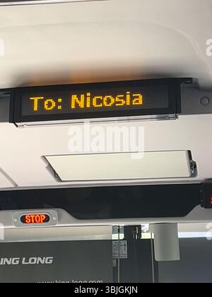 Innenraum eines modernen Busses mit einem hellen LED-Schild, das das Ziel „nach Nicosia“ anzeigt, und einer beleuchteten roten Stopptaste, die während der Tagesfahrt erfasst wird. Stockfoto