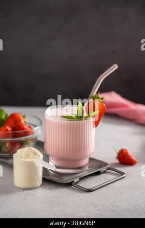 Proteinrosa Erdbeershake in einem Glas und einem Messlöffel Proteinpulver. Stockfoto