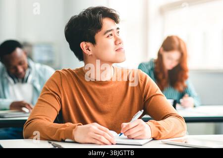 Lächelnder asiatischer Student, der im Klassenzimmer am Schreibtisch sitzt Stockfoto