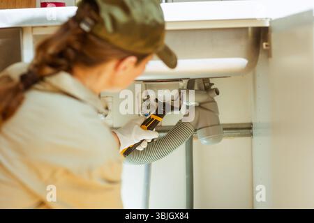 Ein erfahrener Klempner stellt die Abflussrohre unter einem Küchenspüle ein, indem er mit einem verstellbaren Schraubenschlüssel ein Problem mit der Sanitäranlage in der Wohnung löst. Stockfoto