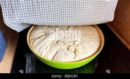 Perfekt gefertigter frischer Hefeteig in einer Schüssel für Brot oder Kuchen, der unter dem Baumwollturm liegt. Roher Hefeteig, der zum Backen ruhen und aufsteigen kann. Hausgemacht Stockfoto