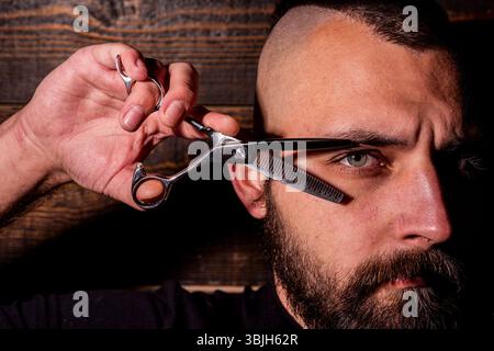 Friseur. Barbier Hand hält Schere. Professionelle Werkzeuge für Friseur. Männlicher Haarschnitt und Bart. Barbier macht Bart für bärtigen Mann im Friseurladen. Friseur Stockfoto
