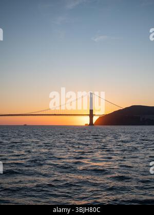 Die Golden Gate Bridge ist von der untergehenden Sonne umgeben, von einem Boot auf dem Wasser aus gesehen. Stockfoto