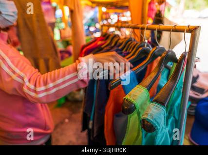 Besucher des lokalen thailändischen Markts stöbern in einer Vielzahl bunter traditioneller Kleidung und Kleidungsstücke, die von ländlichen Händlern ausgestellt werden und authentische handgefertigte Apps anbieten Stockfoto