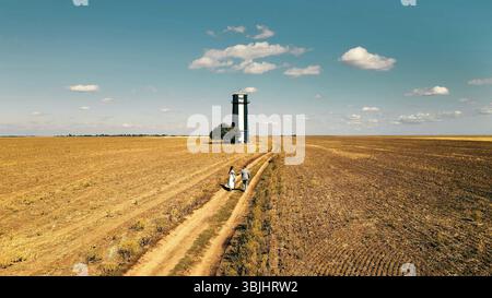 Leuchtturm in einem riesigen Trockenfeld mit ein paar Spaziergängen. Ein weitläufiger Blick auf ein trockenes, karges Feld mit einem Leuchtturm in der Ferne. Stockfoto