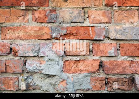 Alte Ziegelmauer mit zerbröckeltem Mörtel. Ein detaillierter Blick auf eine alte Ziegelmauer mit sichtbaren Anzeichen von Verschleiß und zerbröckeltem Mörtel. Stockfoto