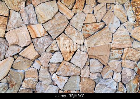 Strukturierte Steinwand mit unregelmäßigen Formen. Ein detailliertes Bild einer strukturierten Steinmauer, die aus unregelmäßig geformten Steinen in verschiedenen Beigetönen besteht Stockfoto