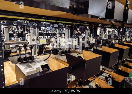 Automatisierte Maschinen befördern Regale in einer Werkstatt und arbeiten an komplizierten schwarzen Objekten. Branche, Technologie und Fertigungsprozess im Fokus Stockfoto