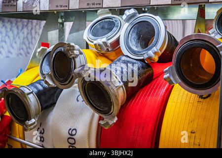 Bunte Feuerwehrschläuche mit Metallkupplungen auf einem Regal. Rote, gelbe und weiße Spiralschläuche, Feuerwehrausrüstung Nahaufnahme Stockfoto