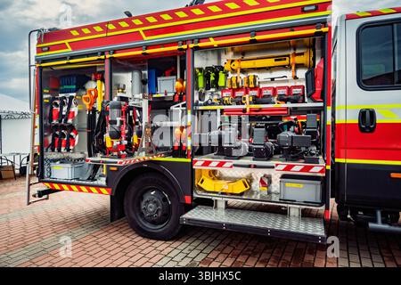 Seitenansicht eines roten Feuerwehrwagens mit offenen Fächern, die detaillierte Löschausrüstung und -Werkzeuge enthalten, bereit für den Notfall- und Rettungsdienst Stockfoto