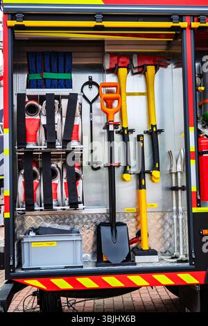 Nahaufnahme eines Feuerwehrwagenabteils, in dem wichtige Löschausrüstung, einschließlich Schläuche, Äxte, Schaufel und Rettungswerkzeuge, ausgestellt ist; bereit für die Zukunft Stockfoto