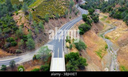 Winding Road durch Dry und Green Hills. Ein Blick aus der Vogelperspektive auf eine gewundene Straße, die sich durch eine Landschaft aus trockenen Hügeln und grünen Flecken schlängelt. Stockfoto