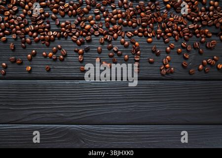 Verstreute Kaffeebohnen auf dunklem Holzhintergrund. Eine Sammlung gerösteter Kaffeebohnen, die auf einem dunklen Holzhintergrund verstreut sind, unterstreicht die Stockfoto