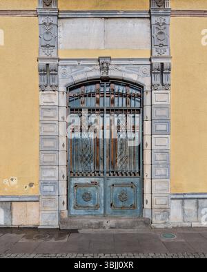 Architektonisches Detail der verzierten blauen Metalltür mit dekorativem Eisen, Rost und geschnitztem Steinrahmen auf gelbem Gebäude Stockfoto