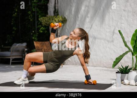 Fitte Frau, die im Freien mit Hanteln und Handgelenkgewichten trainieren, Stärke, Gleichgewicht und aktives gesundes Leben zeigen. Stockfoto