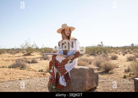 Frau im Festivalkleid sitzt auf Felsen in Wüstenzeichnung Stockfoto